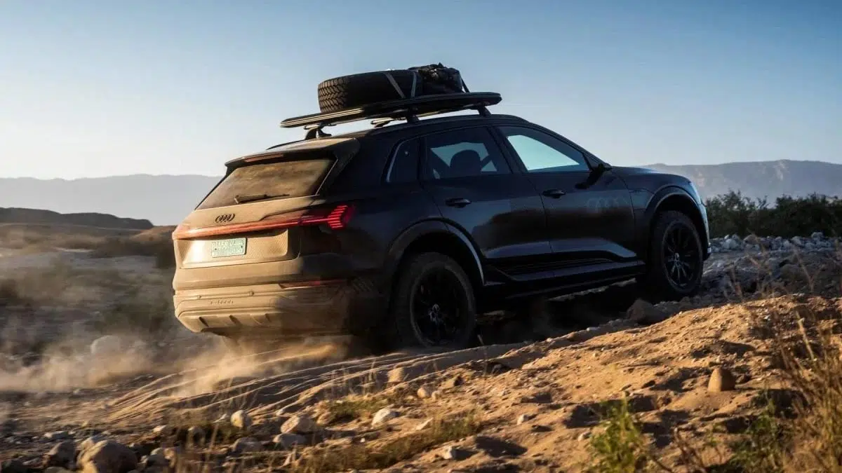 Vista trasera del Audi Q6 e-tron todoterreno, mostrando sus luces LED y su bodega de techo, en un sendero rocoso.